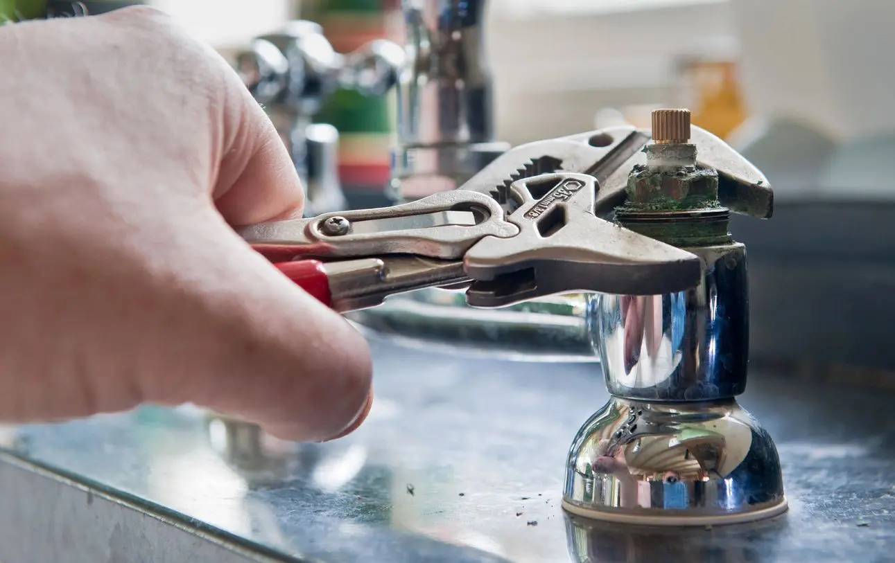 A person is holding a pair of pliers over the top of a faucet.